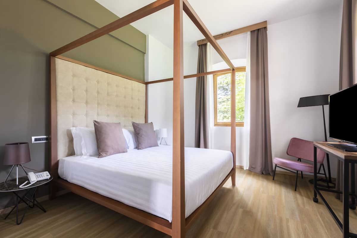 Una cama con dosel y un tablero de cabecera acolchado, una mesita de noche con lámpara, teléfono y una silla.
