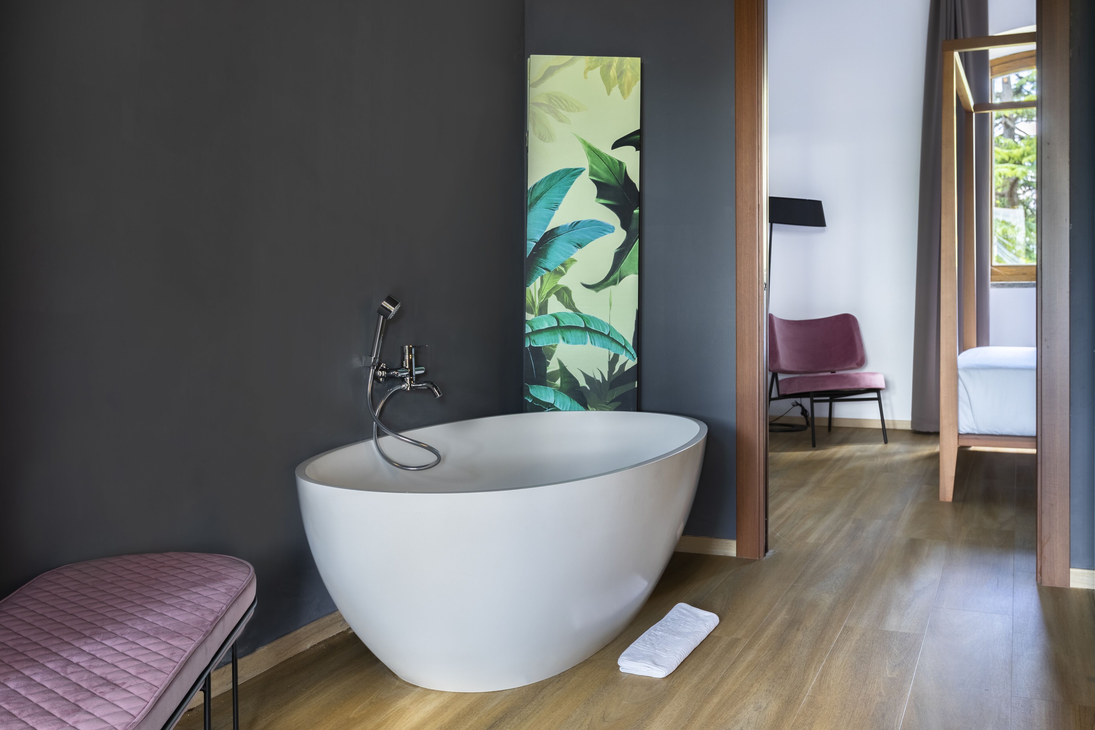 Une salle de bain moderne avec une grande baignoire sur pieds, un banc rose et une grande estampe représentant des motifs végétaux accrochée au mur.