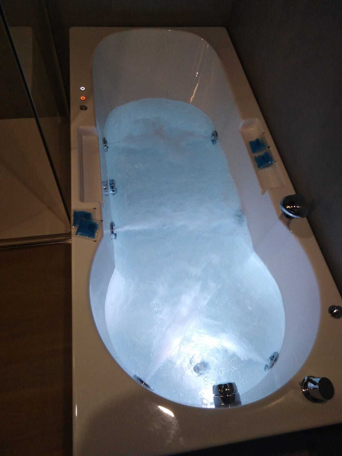Una bañera con panel de vidrio, cabezal de ducha y grifo.