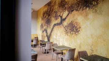 A restaurant with a mural of a tree on the wall, tables, and chairs.