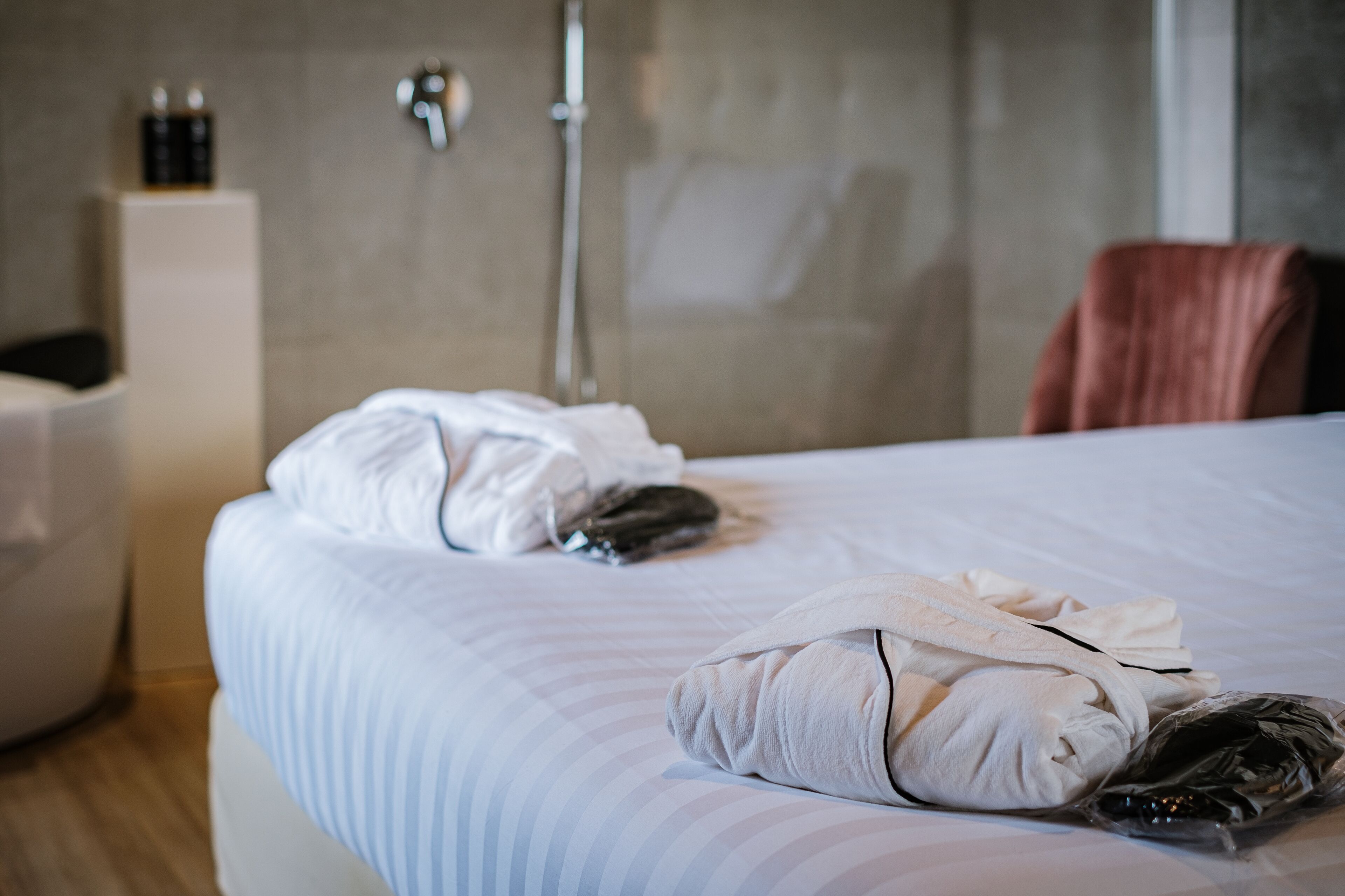 A hotel room with a bed, a towel, a robe, and a shower area.