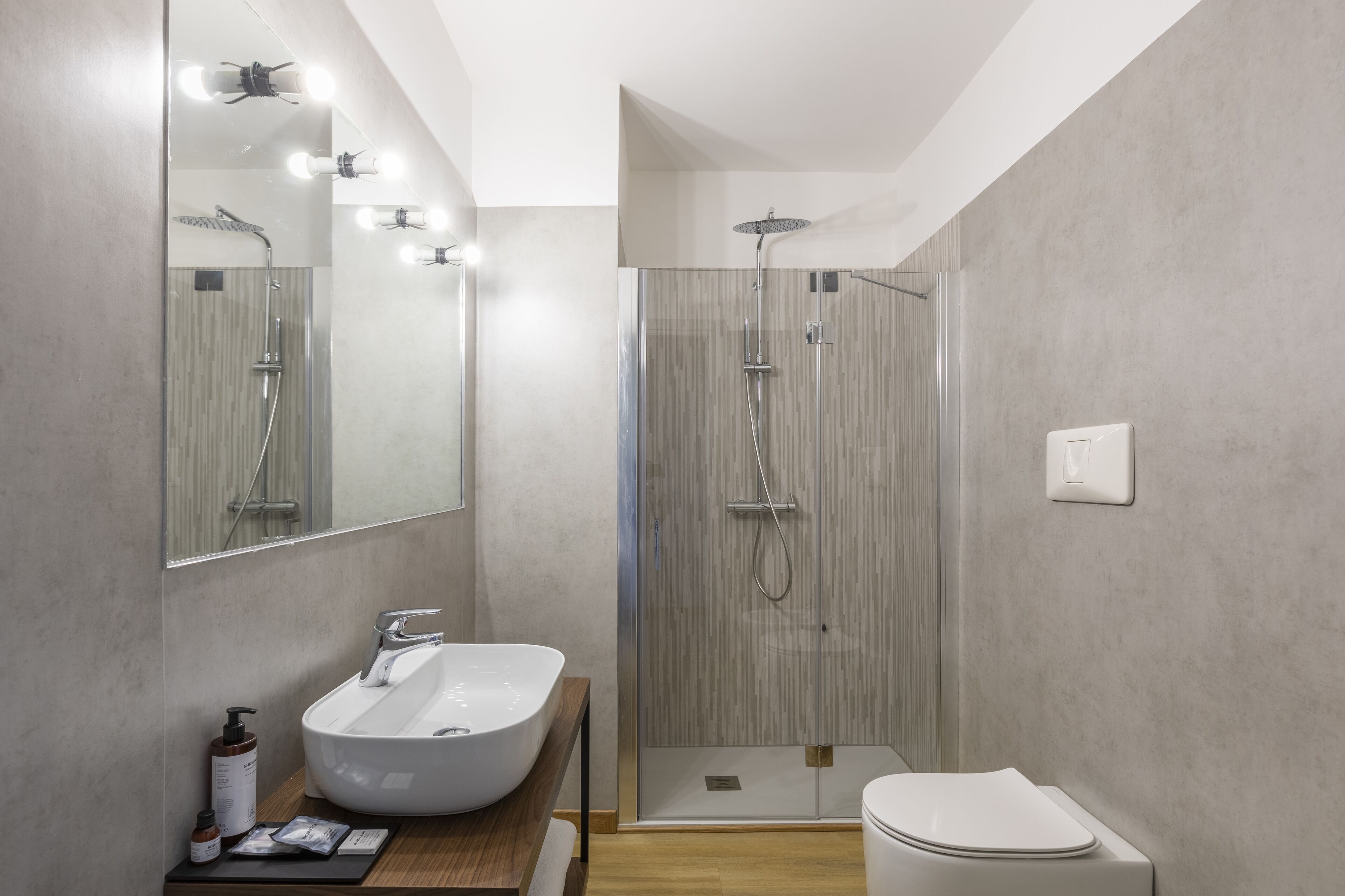 Une salle de bain moderne avec un grand miroir, un lavabo blanc, une cabine de douche et des toilettes.