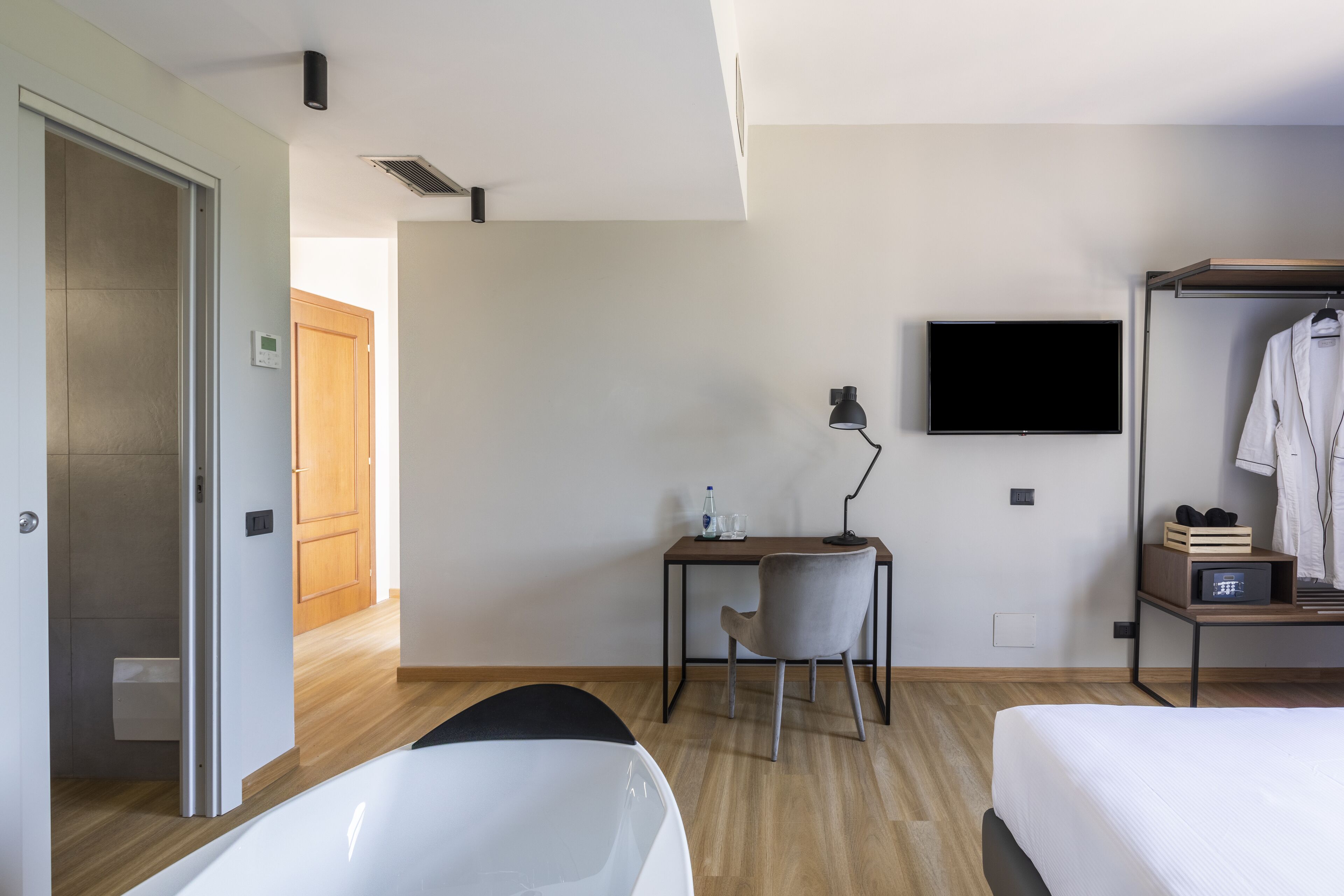 A hotel room with a bed, a desk with a chair, a TV, and a wardrobe.