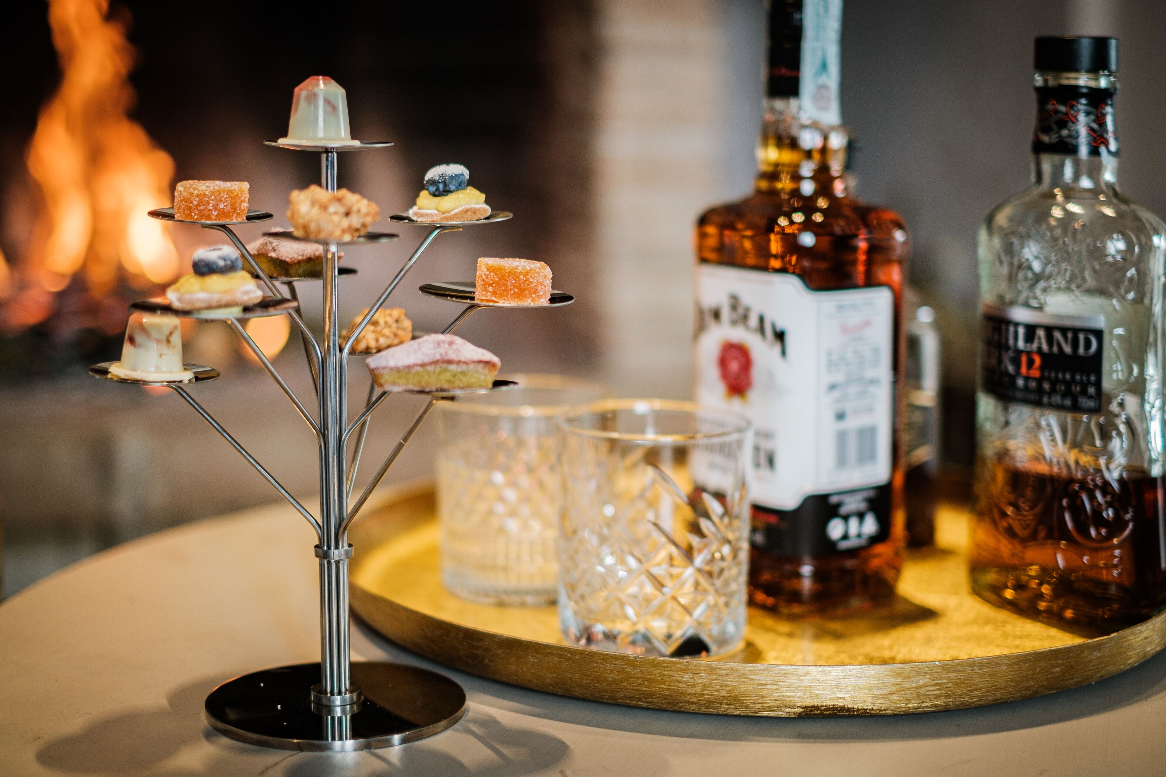 A tray with a dessert stand, two bottles of liquor, and a glass.