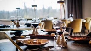 Una mesa de comedor dispuesta con copas de vino, platos y cubiertos, con vistas a árboles a través de una ventana.
