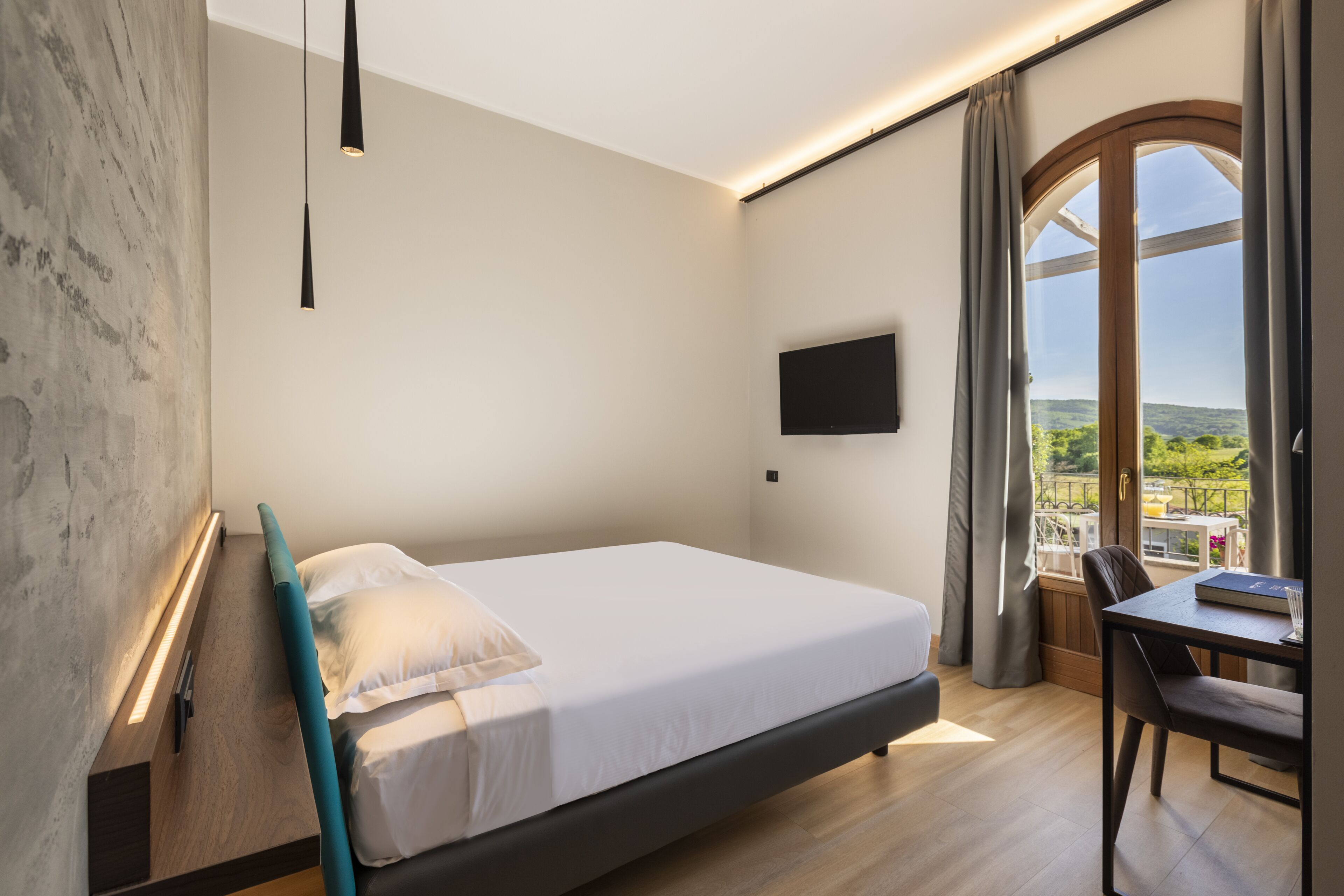 Ett modernt hotellrum med en säng, ett skrivbord och ett stort fönster med utsikt över grönområden.