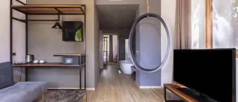 Una sala de estar moderna con un sofá, un televisor sobre un mueble de madera, un columpio colgante y vistas al exterior a través de una ventana.