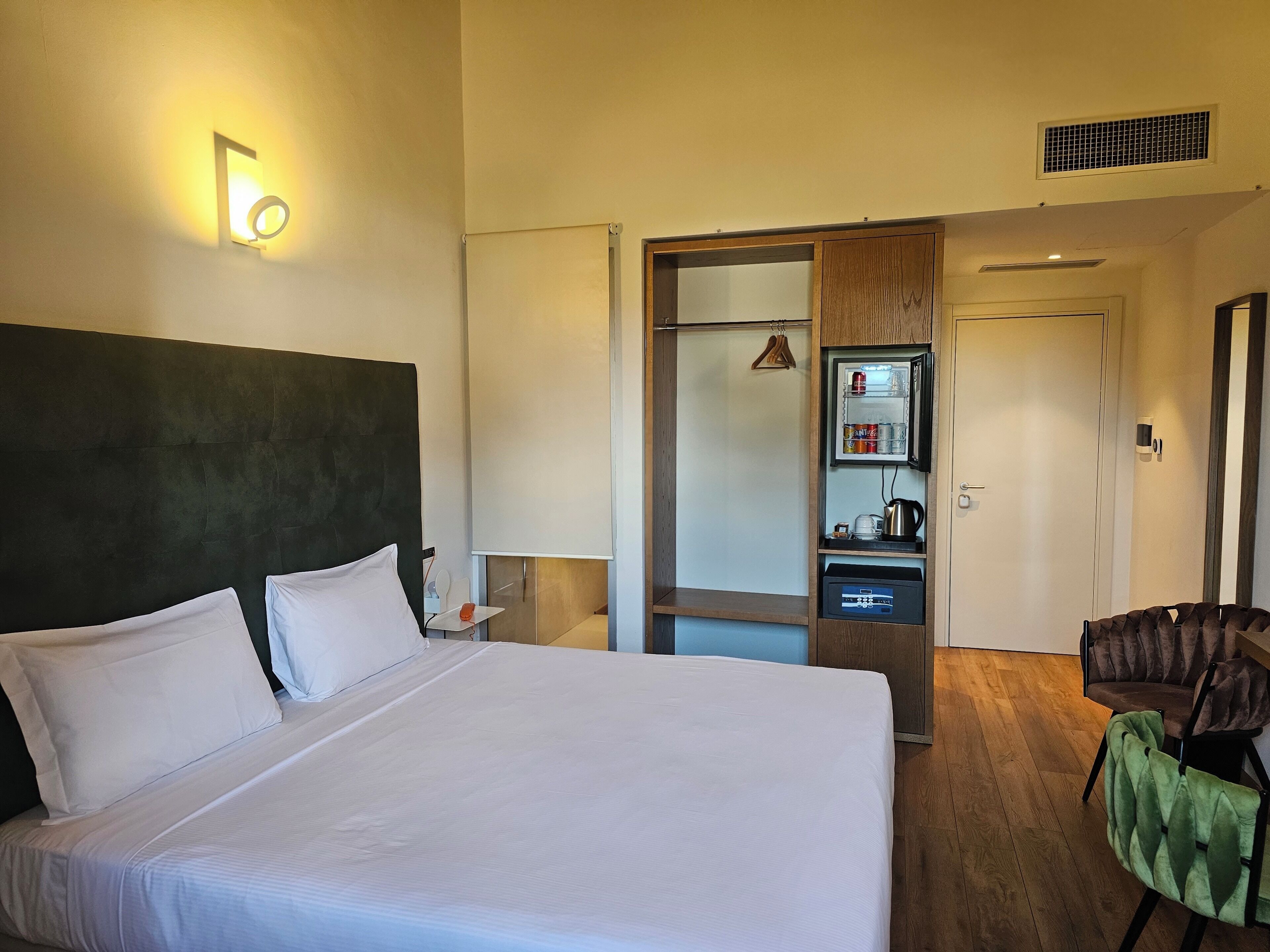 Une chambre d’hôtel avec un grand lit, une armoire, un miroir, une petite table et une chaise.