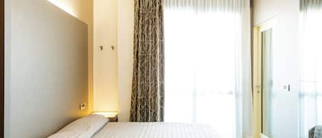 A hotel room with a large bed, a window with curtains, and a door leading to a balcony.