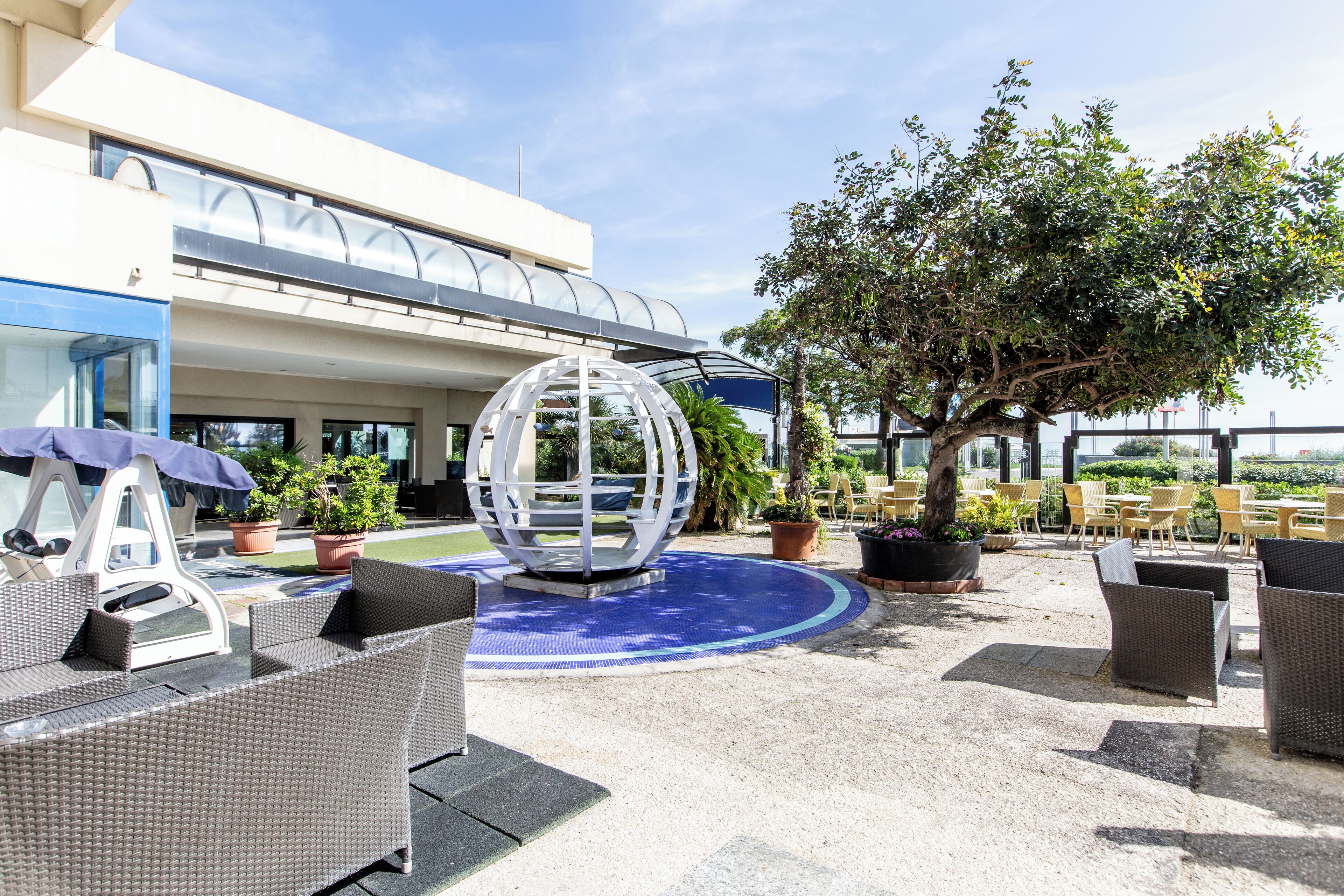 An outdoor patio area with wicker furniture, a spherical decorative piece, and potted plants.