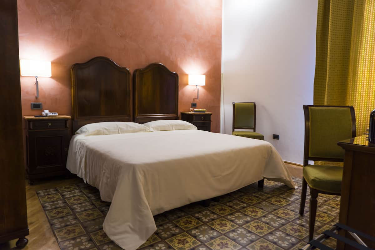 A hotel room with a large bed, two bedside lamps, a chair, a small table, and a mirror.