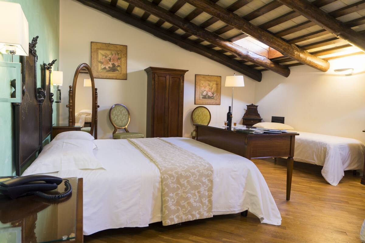 A hotel room with a wooden ceiling, a bed with a white bedspread, a desk with a lamp, and a telephone.