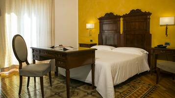 A hotel room with a wooden bed, two bedside tables, a desk with a chair, and a large mirror.