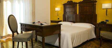 A hotel room with a wooden bed, two bedside tables, a desk with a chair, and a large mirror.