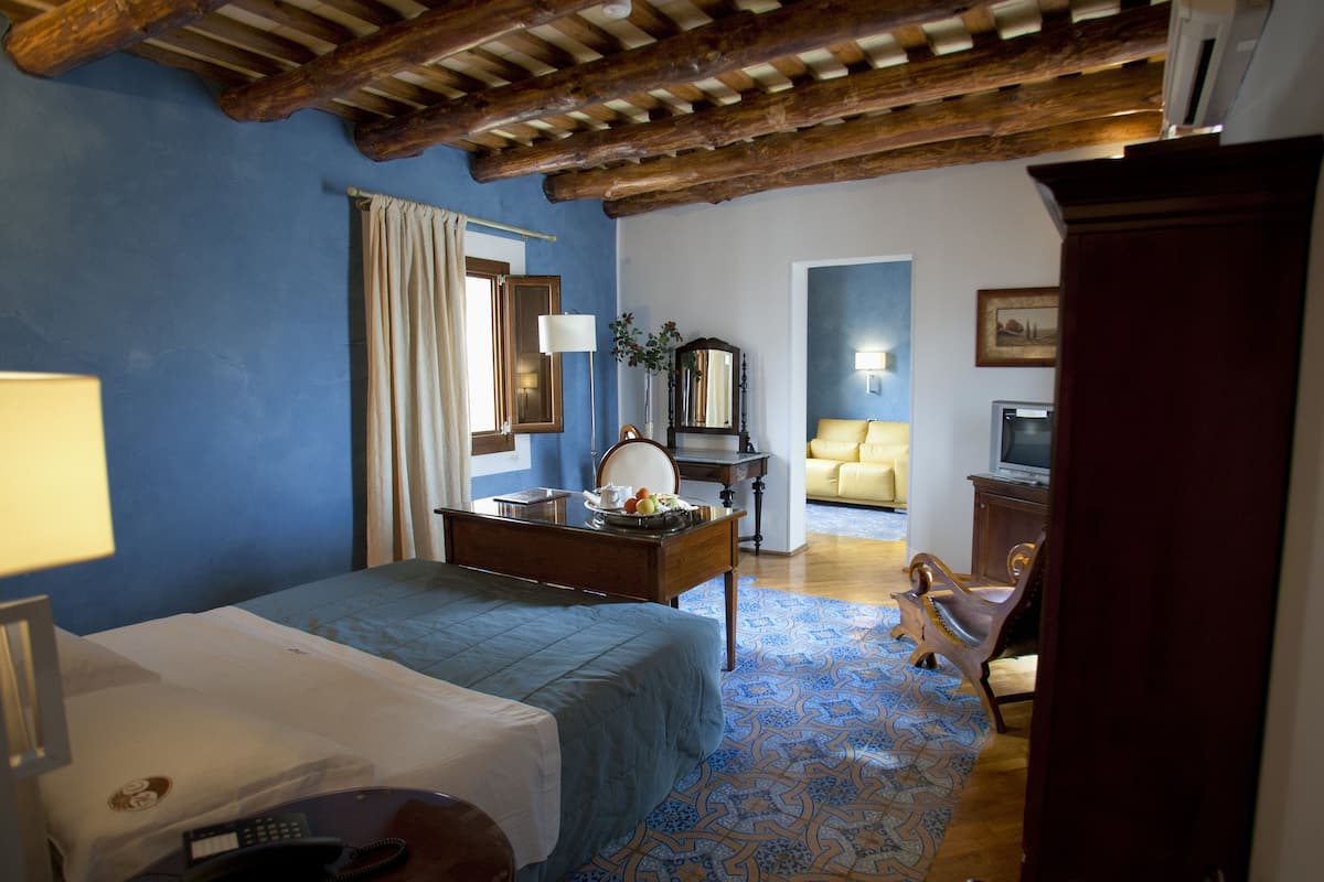 A hotel room with a bed, a desk with a lamp, a chair, a sofa, and a television.