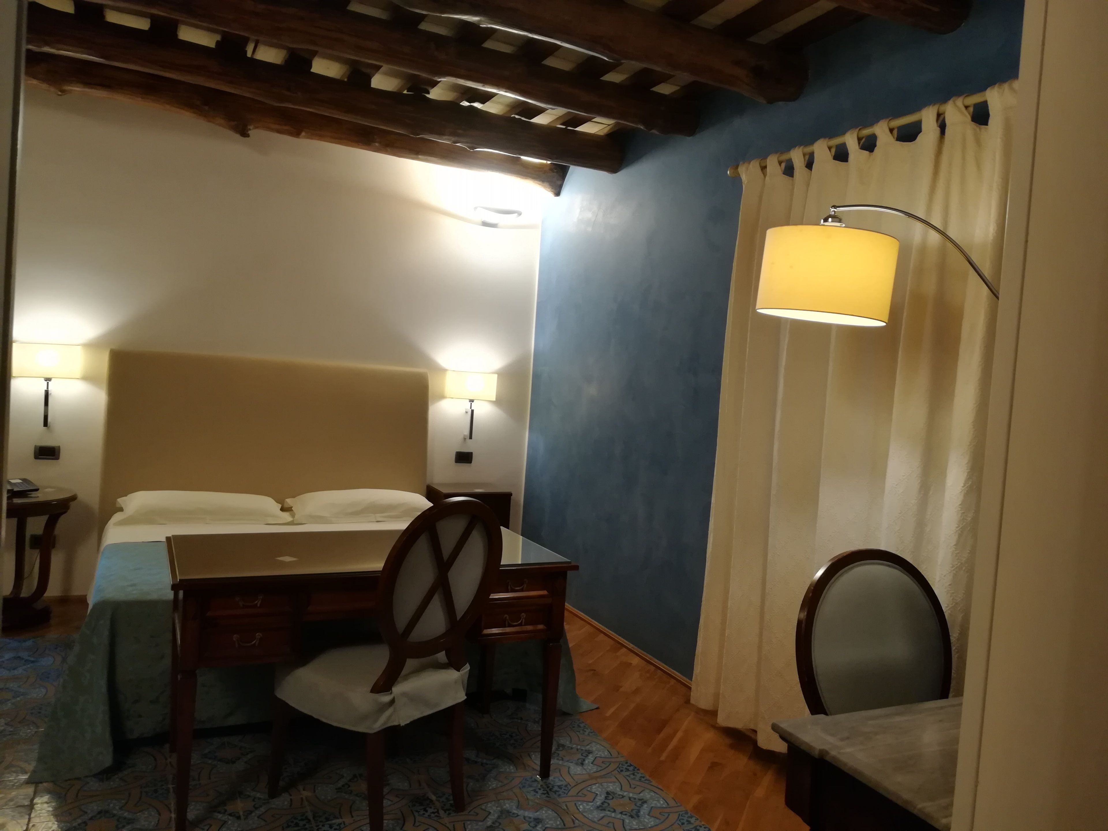 A hotel room with a bed, a desk with a chair, a table, and a lamp.
