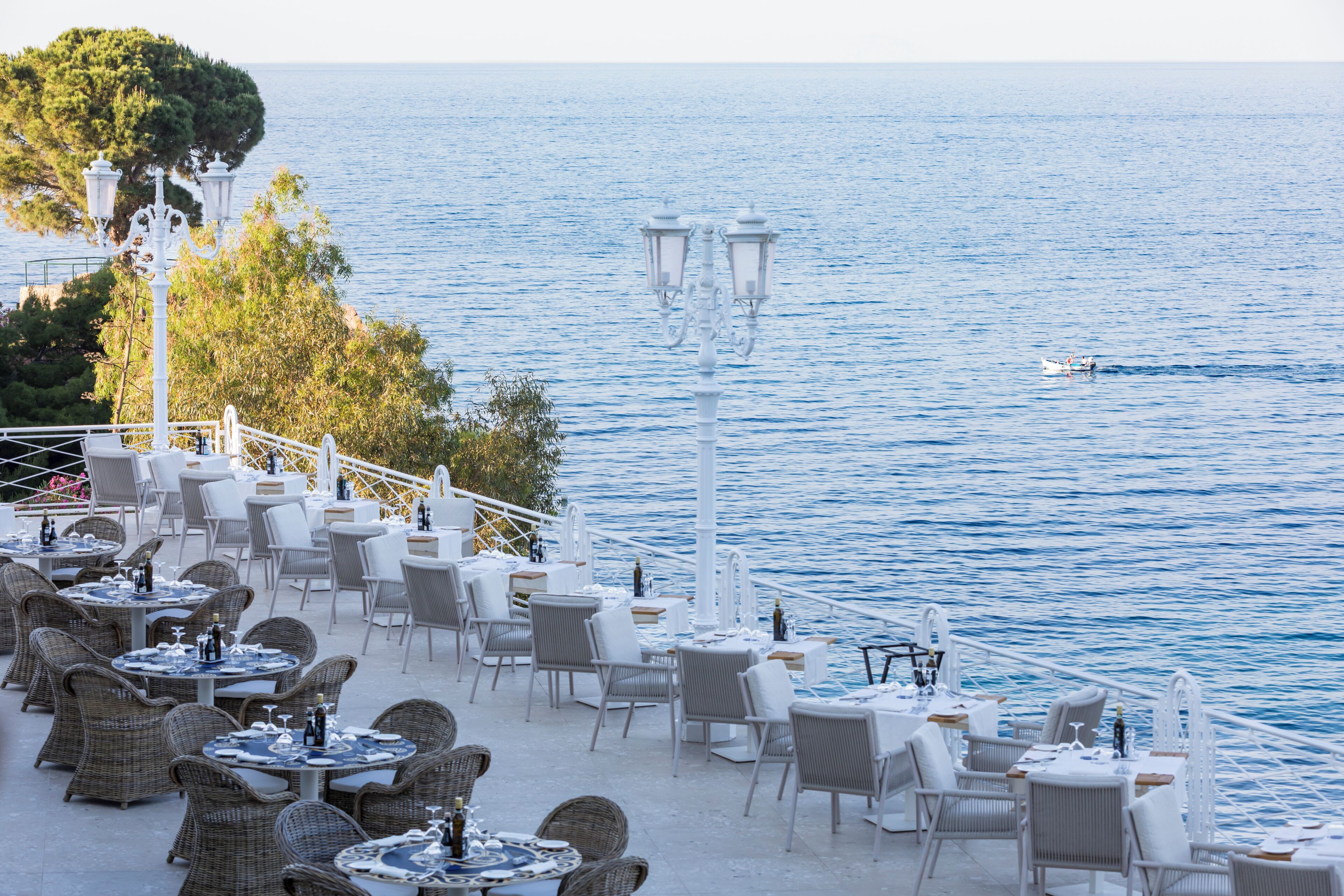 An outdoor dining area with tables and chairs, overlooking a body of water.
