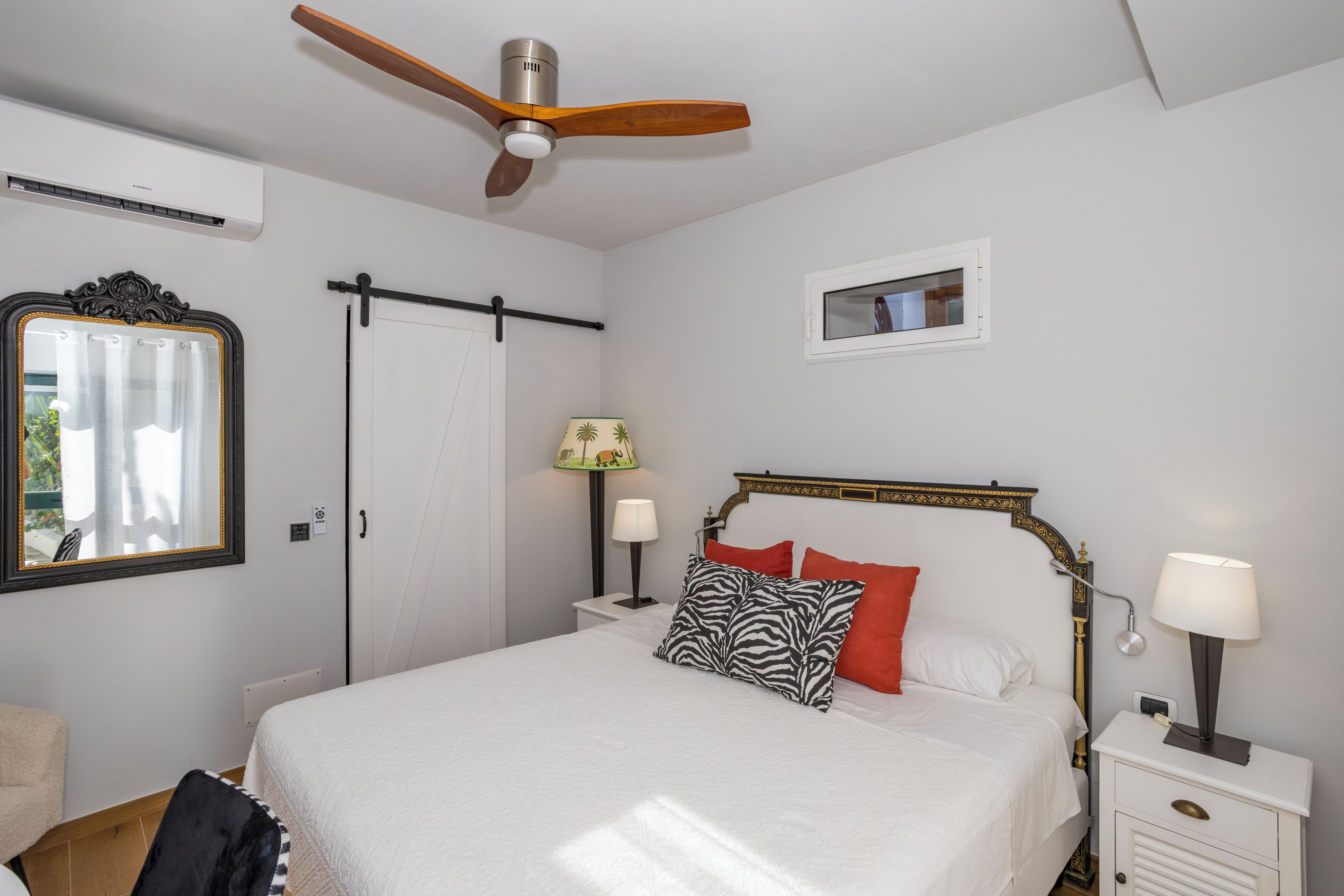A bedroom with a bed, nightstands, a ceiling fan, a mirror, a window, and a door.