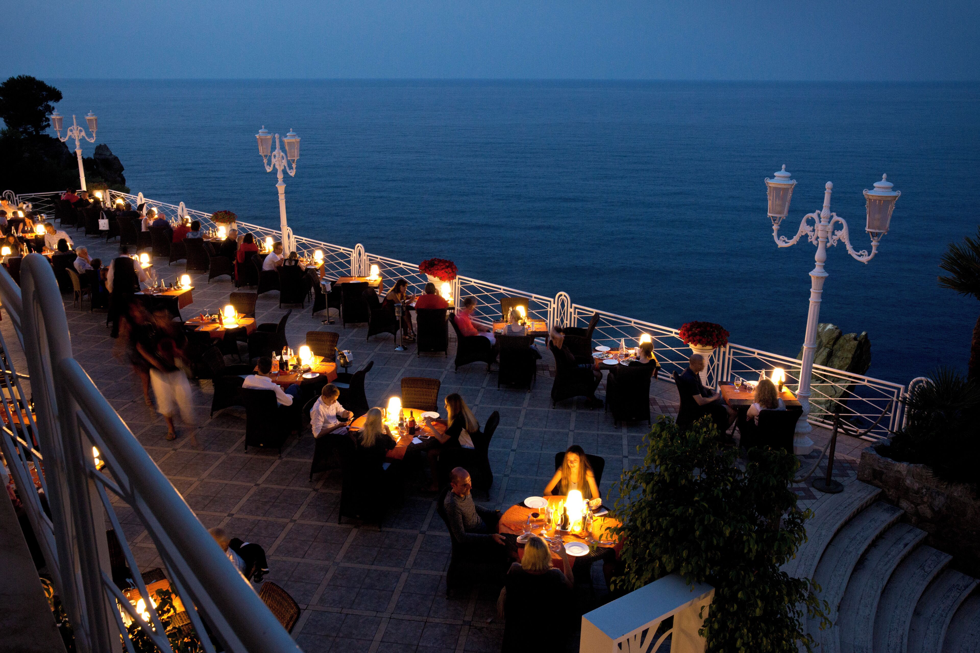 An outdoor dining area with tables and chairs, overlooking the sea.