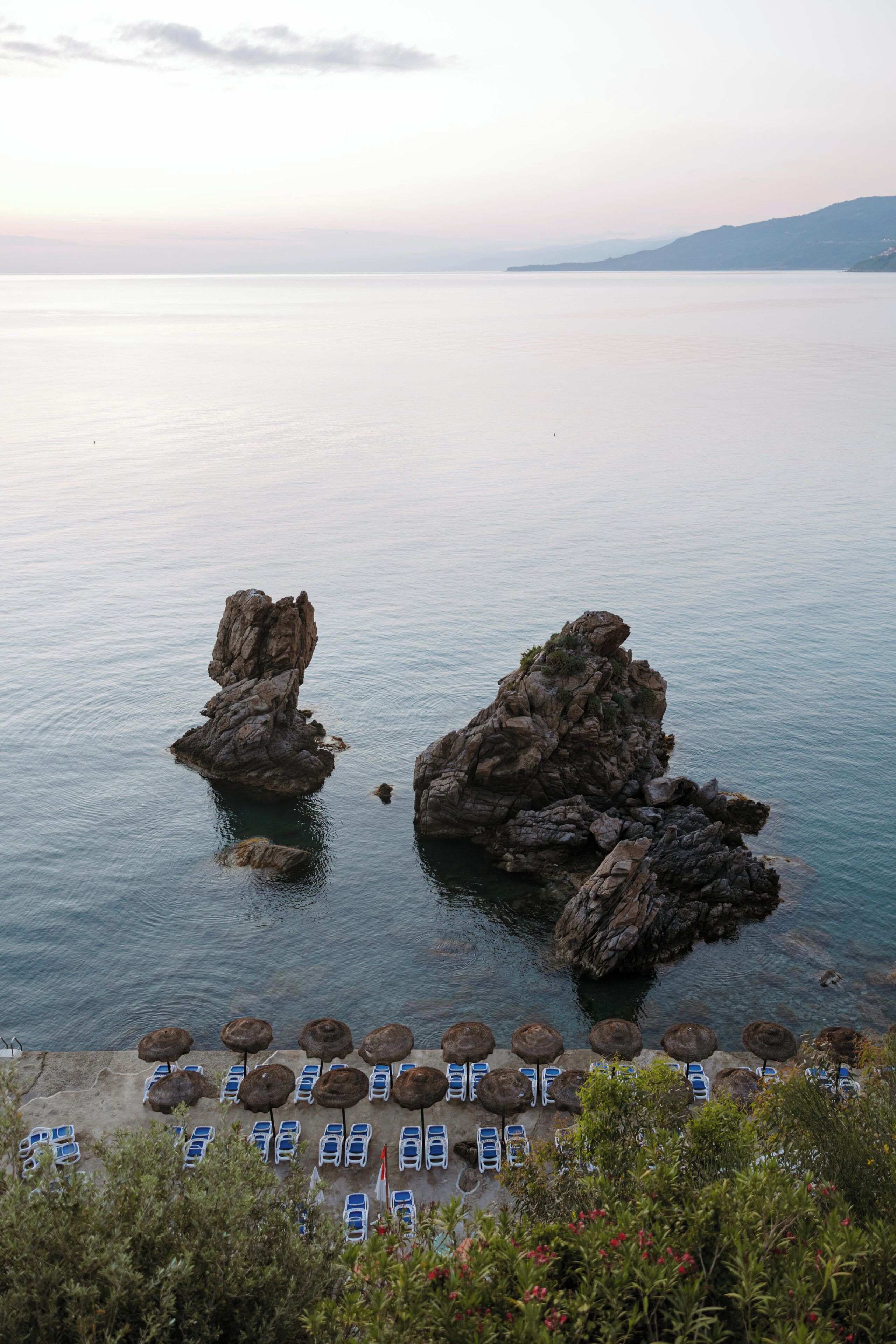A coastal scene with rocky formations and a row of sun loungers facing the sea.
