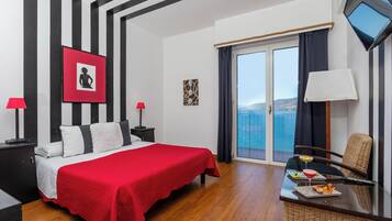 A hotel room with a bed, a TV, a balcony with a view, and a dining table with a chair.