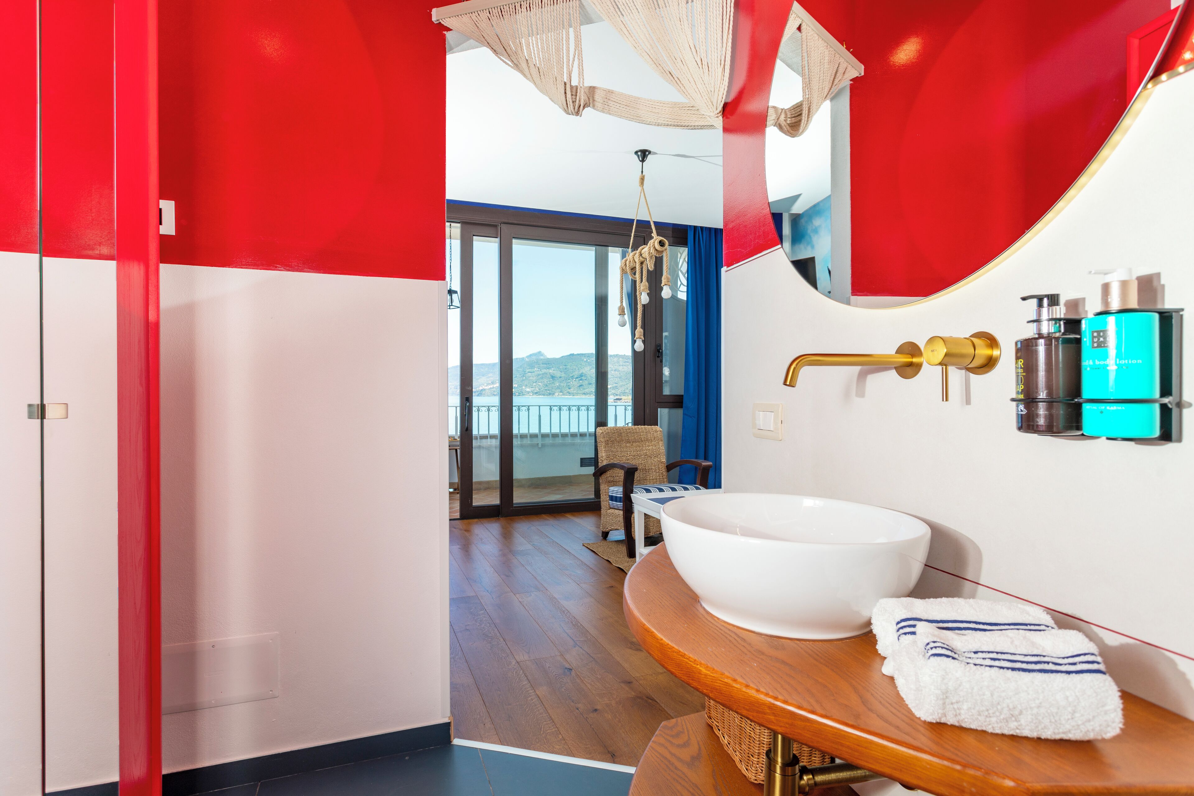 Un baño moderno con un lavamanos grande de color blanco, un mueble de tocador de madera y una decoración en tonos rojo y blanco.