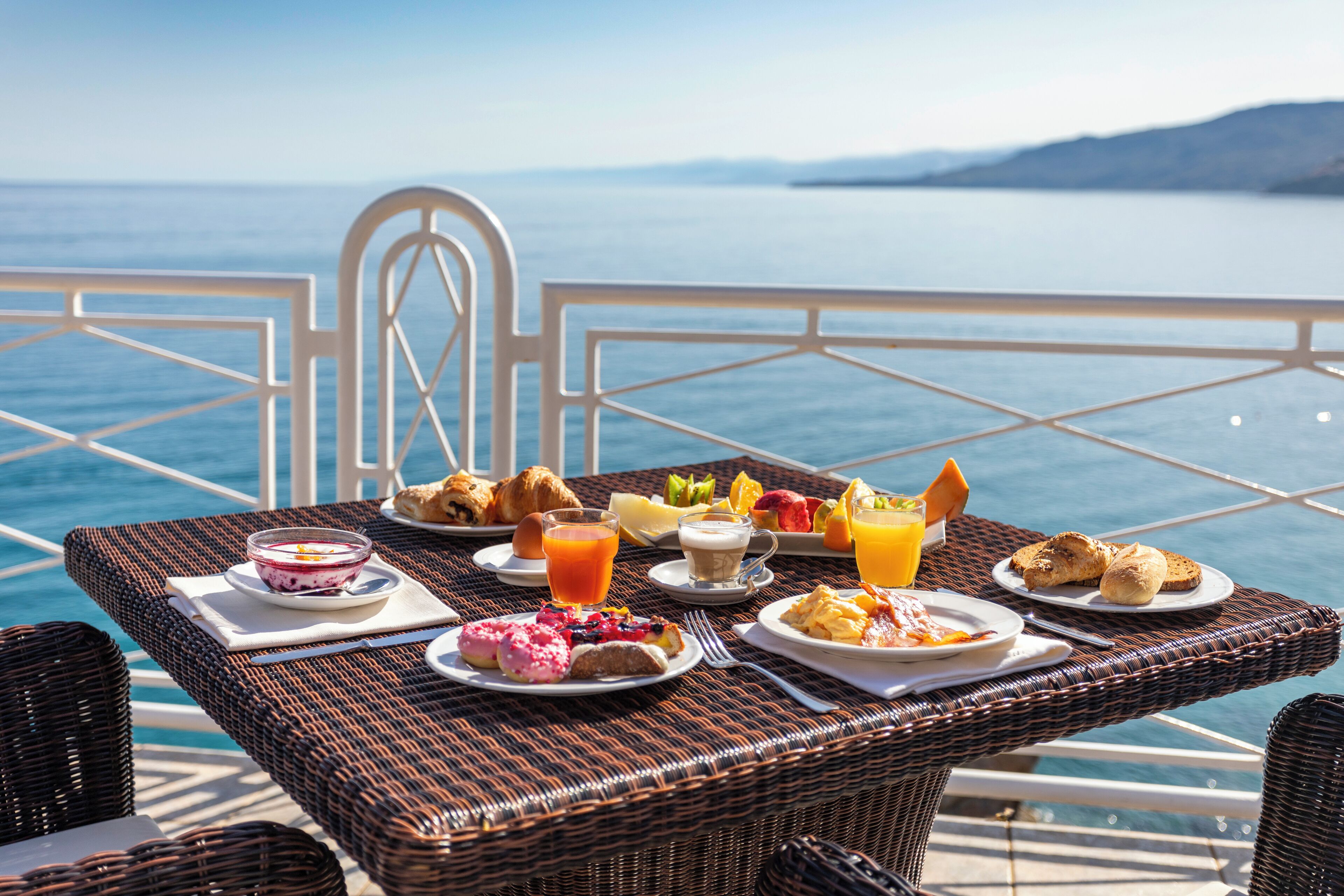 Una mesa de mimbre con comida para el desayuno y vista al mar.