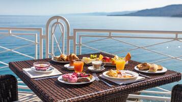 Una mesa de mimbre con comida para el desayuno y vista al mar.