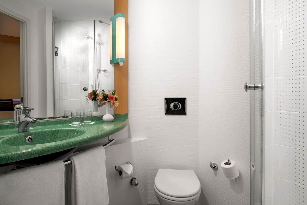 A bathroom with a green countertop sink, a white toilet, a towel rack, and a mirror.