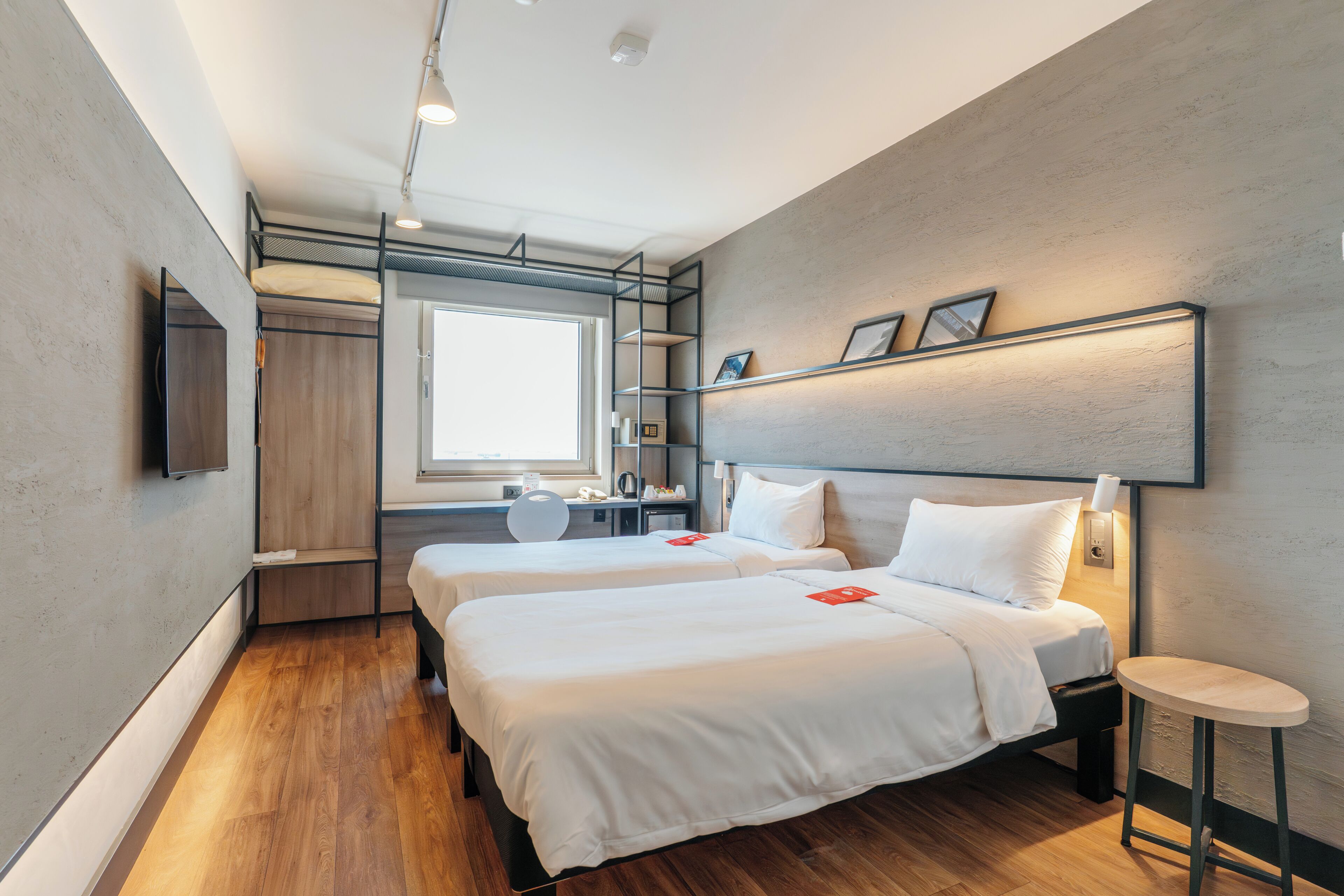 A modern hotel room with two beds, a desk, a chair, a TV, and a window.