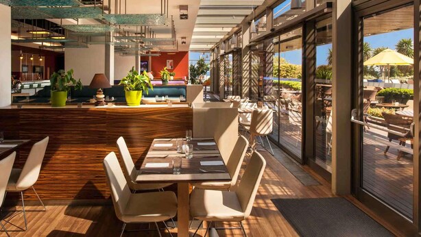 A modern restaurant with a glass ceiling, wooden flooring, and outdoor seating with umbrellas. - Ibis Istanbul Zeytinburnu (Istanbul)