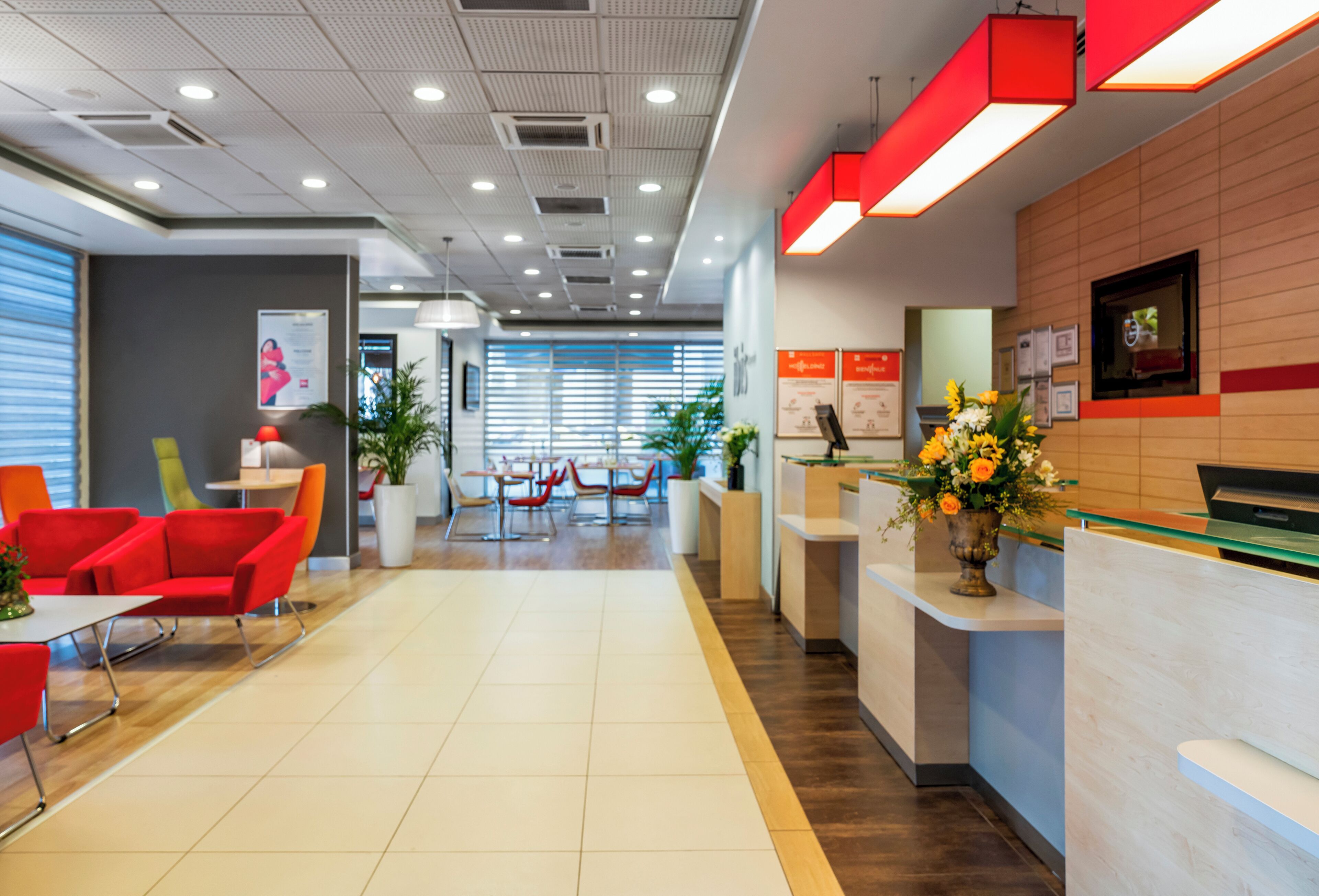 A modern reception area with a reception desk, red and orange seating, and a potted plant.