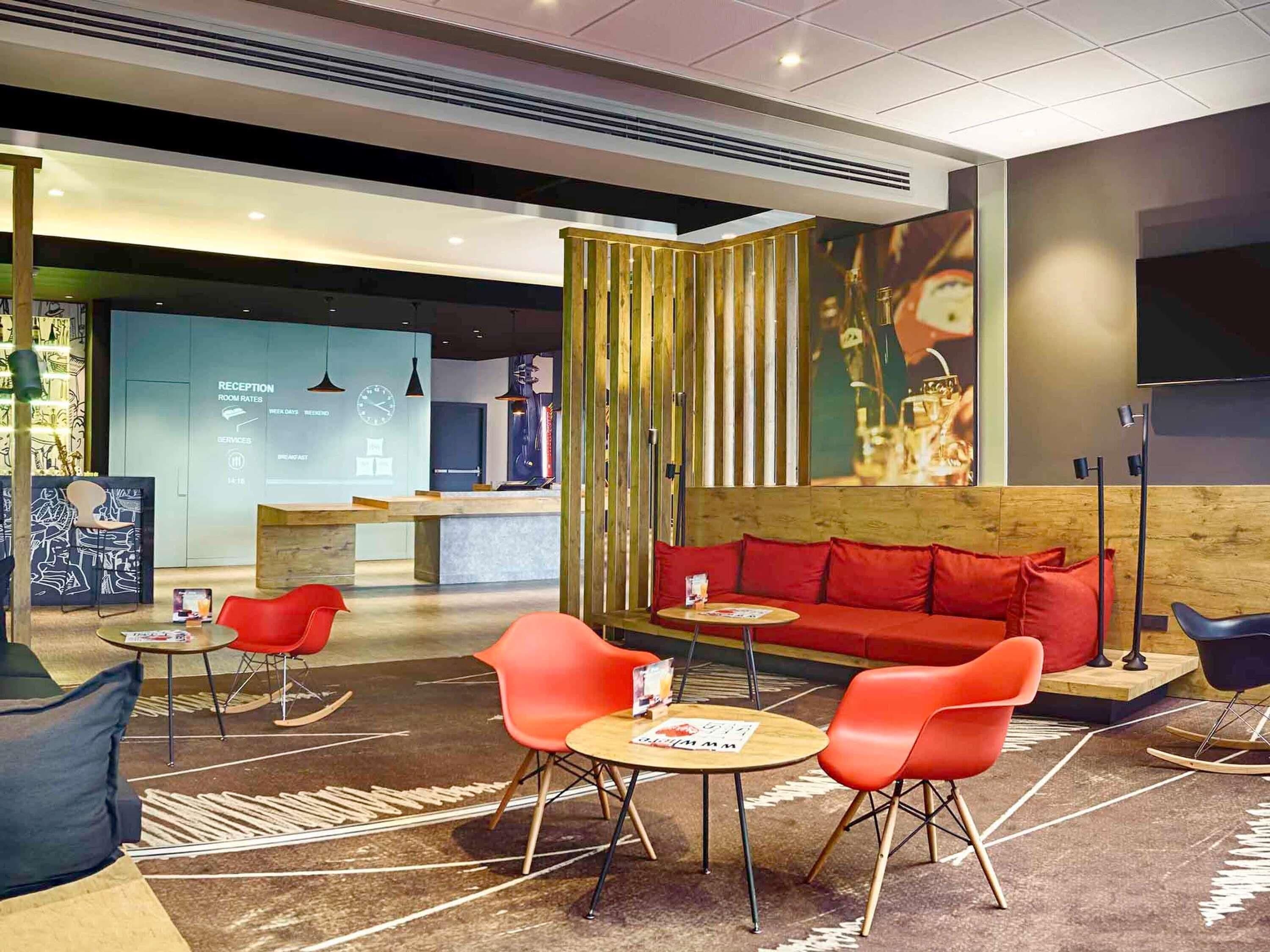 A modern hotel lobby with a reception desk, a red sofa, and orange chairs.