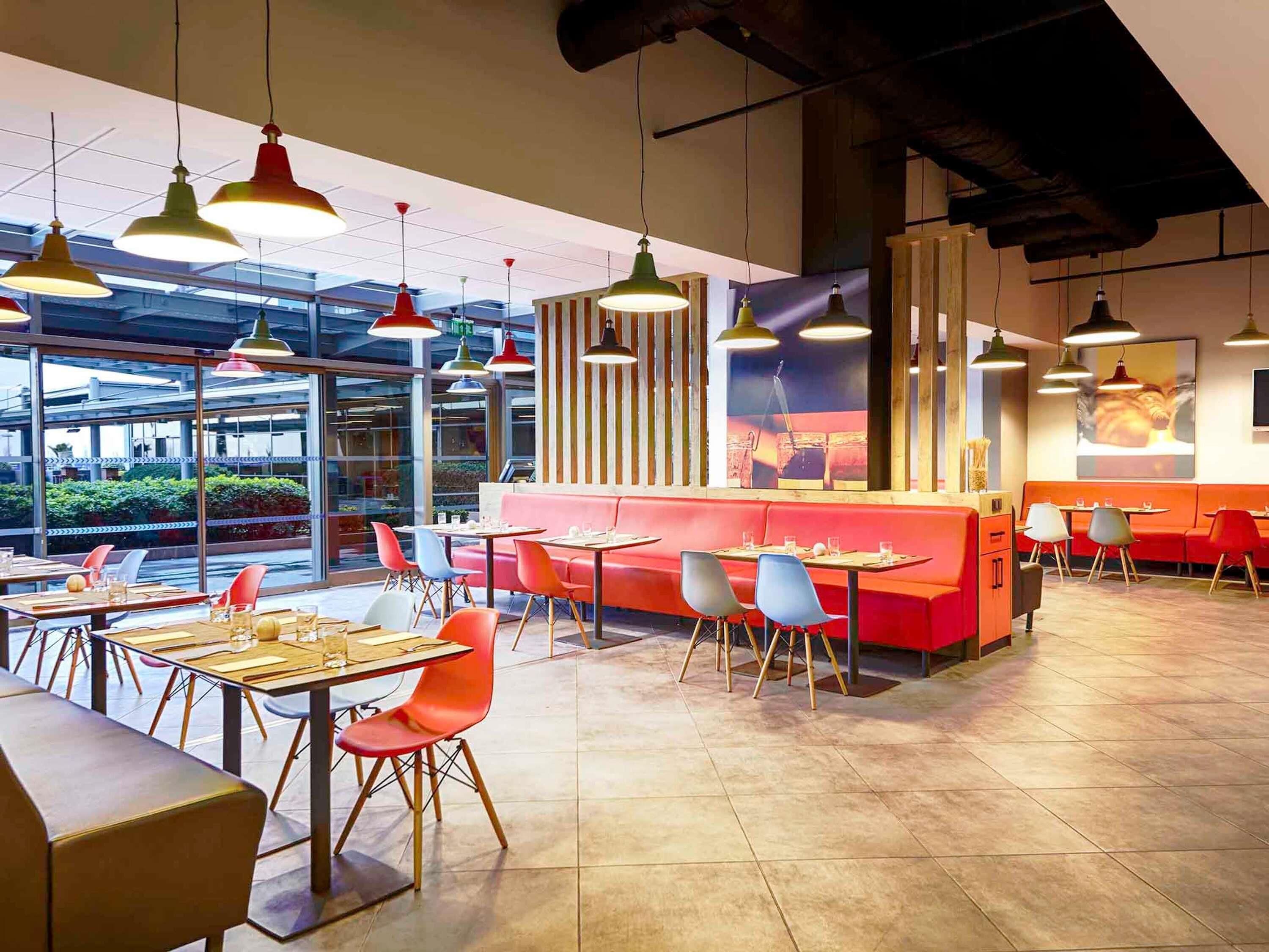 Un intérieur de restaurant moderne avec plusieurs espaces de restauration, des chaises colorées et des luminaires suspendus.