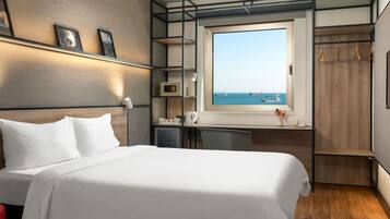 Ein modernes Hotelzimmer mit Bett, Schreibtisch, Kleiderschrank und einem Fenster mit Meerblick.
