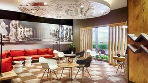 A modern interior with a red sofa, white chairs, a round table, and a chess-themed wall. - Ibis Istanbul Zeytinburnu (Istanbul)