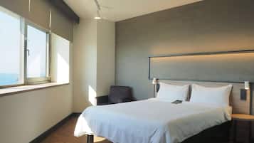 Ein modernes Hotelzimmer mit einem großen Bett, einem Sessel, einem kleinen Tisch und Meerblick durch ein großes Fenster.