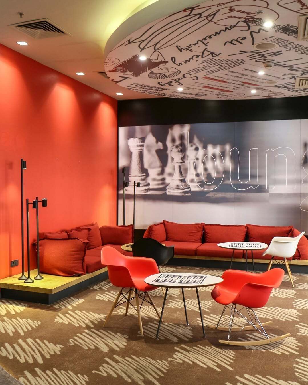Un'area lounge moderna con divani rossi, una scacchiera e un'ampia parete con dediche.