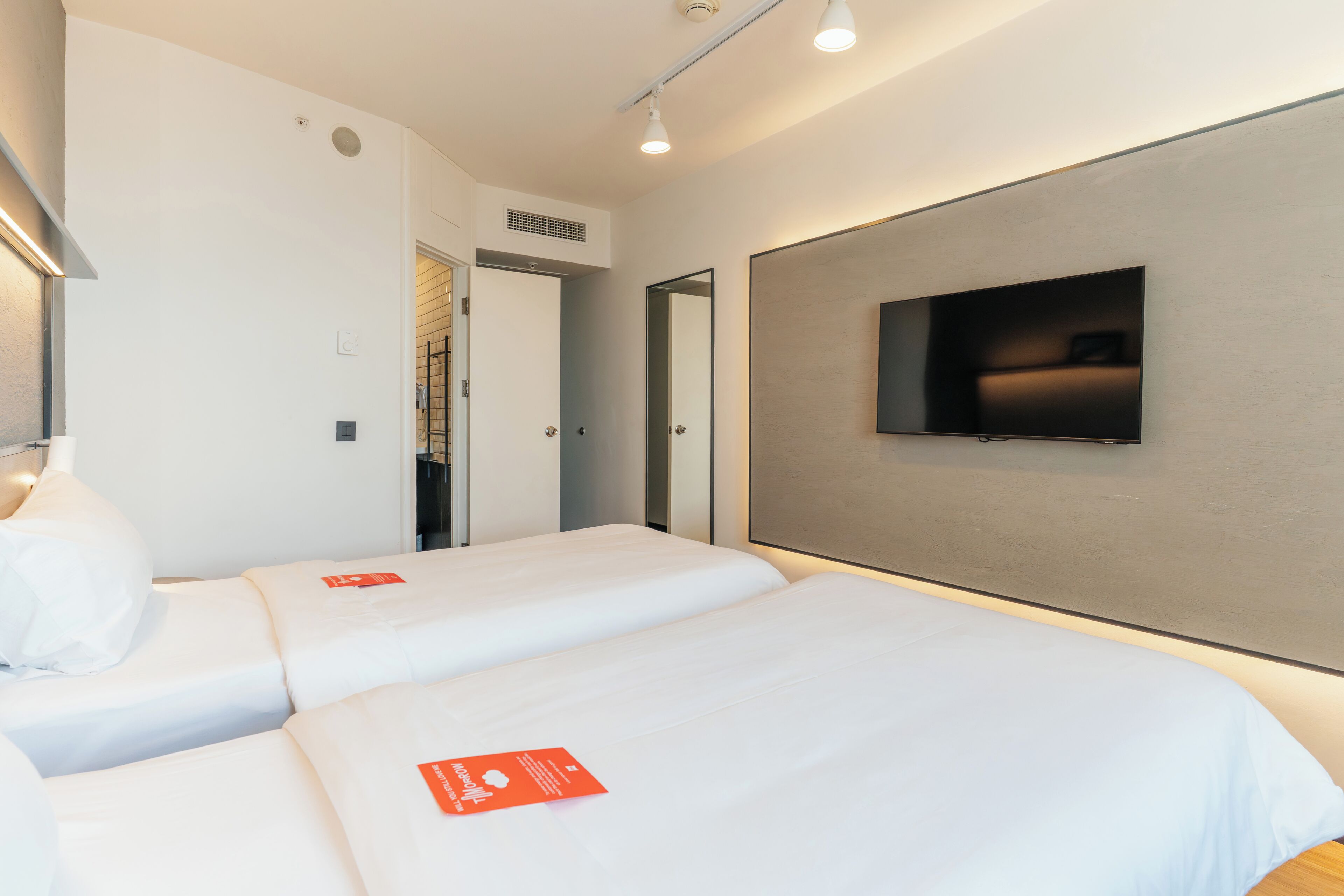 A hotel room with two beds, a flat-screen TV mounted on the wall, and a door leading to another room.