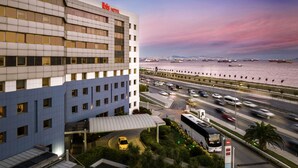 A modern hotel with a prominent "ibis hotel" sign, a waterfront view, and a busy road with vehicles. - Ibis Istanbul Zeytinburnu (Istanbul)