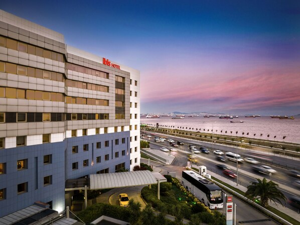 A modern hotel with a prominent "ibis hotel" sign, a waterfront view, and a busy road with vehicles. - Ibis Istanbul Zeytinburnu (Istanbul)