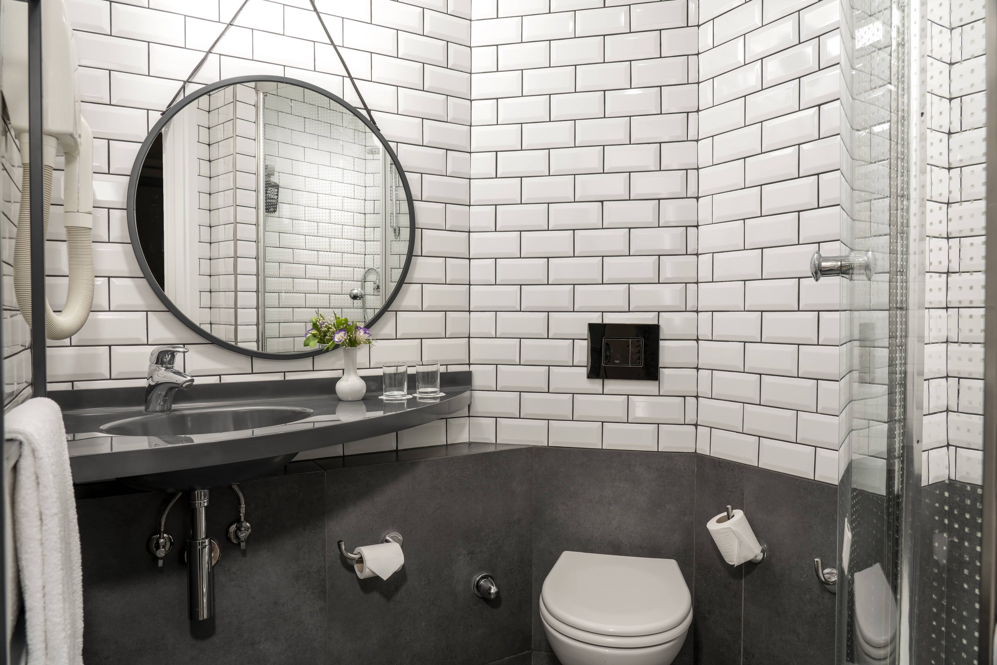 A modern bathroom with a black sink, white tiles, a round mirror, and a toilet.