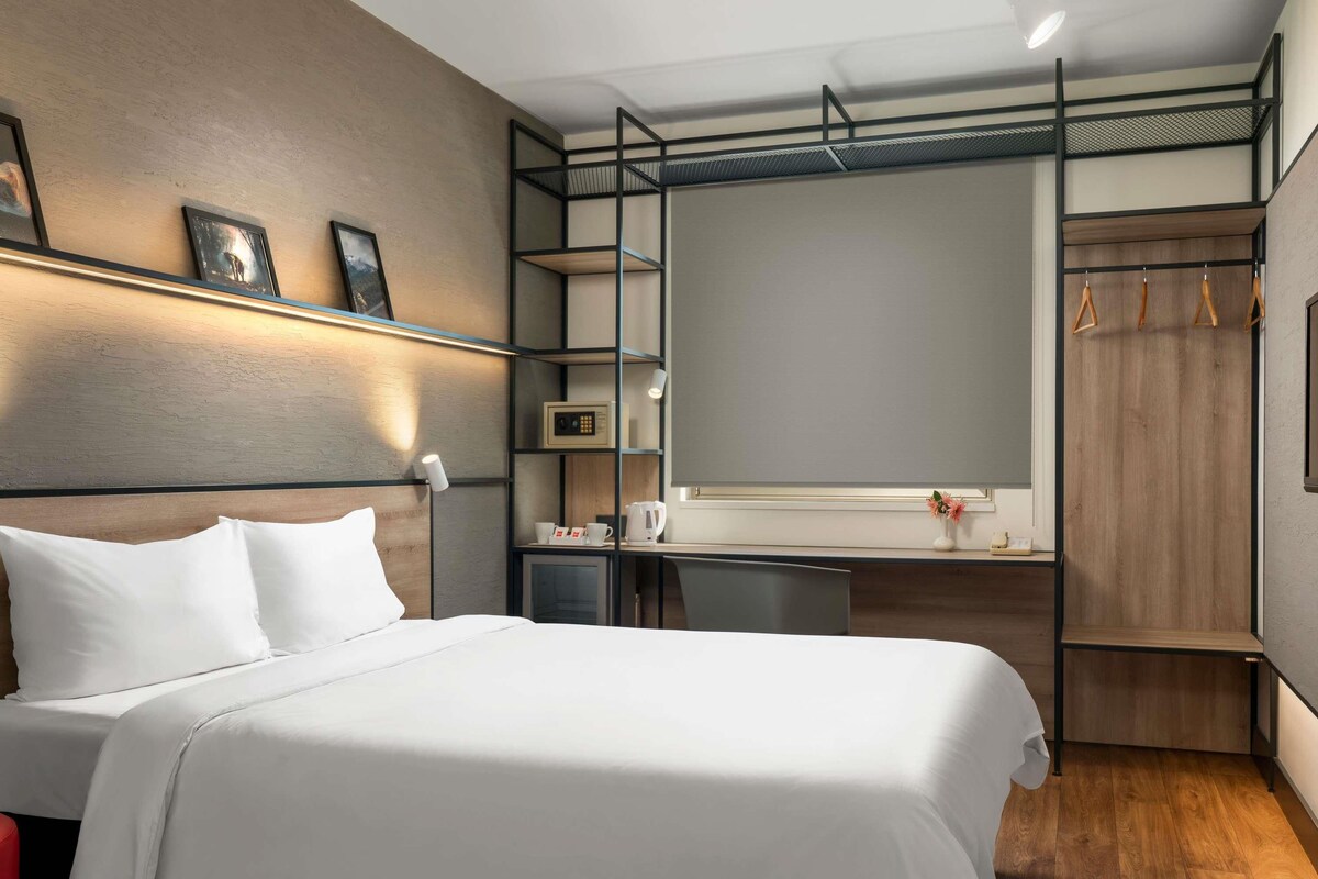 A modern hotel room with a bed, desk, wardrobe, and a large mirror.