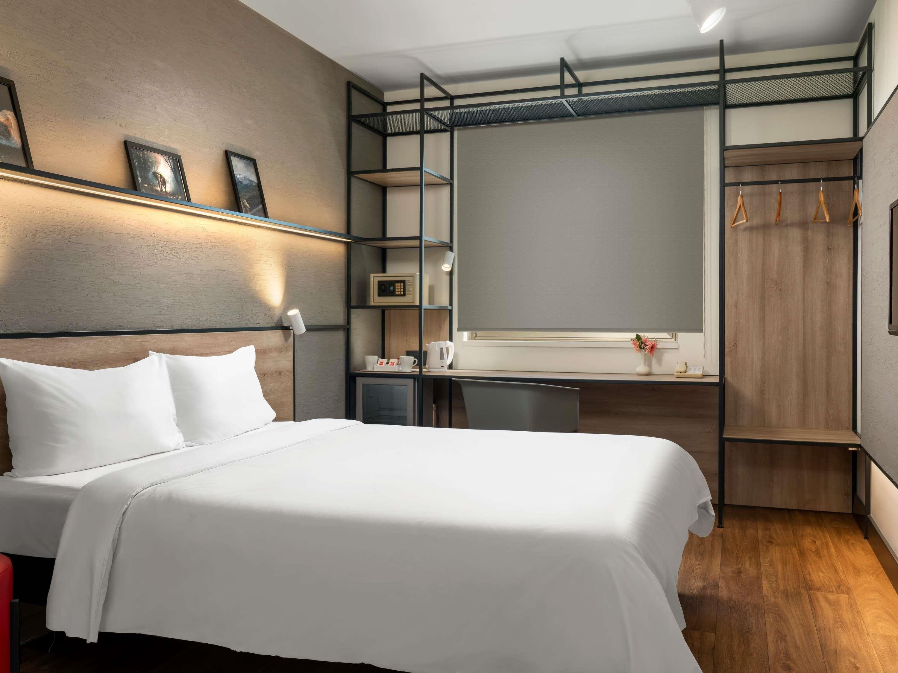 A modern hotel room with a bed, desk, wardrobe, and a large mirror.