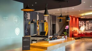A modern reception desk with a wooden counter, black pendant lights, and a digital clock. - Ibis Istanbul Zeytinburnu (Istanbul)