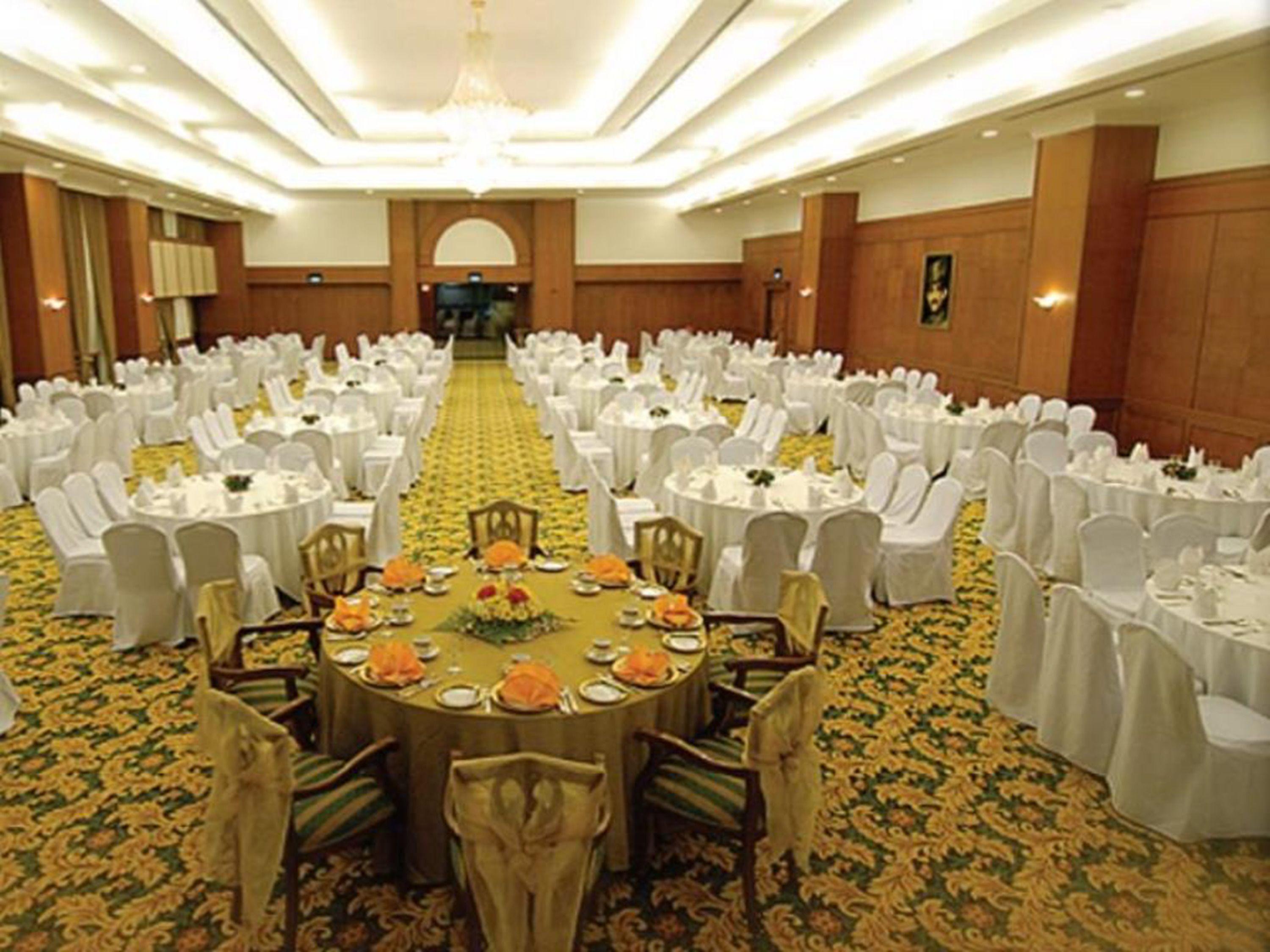 Une salle de banquet avec des tables rondes, des chaises blanches et un sol recouvert de moquette.