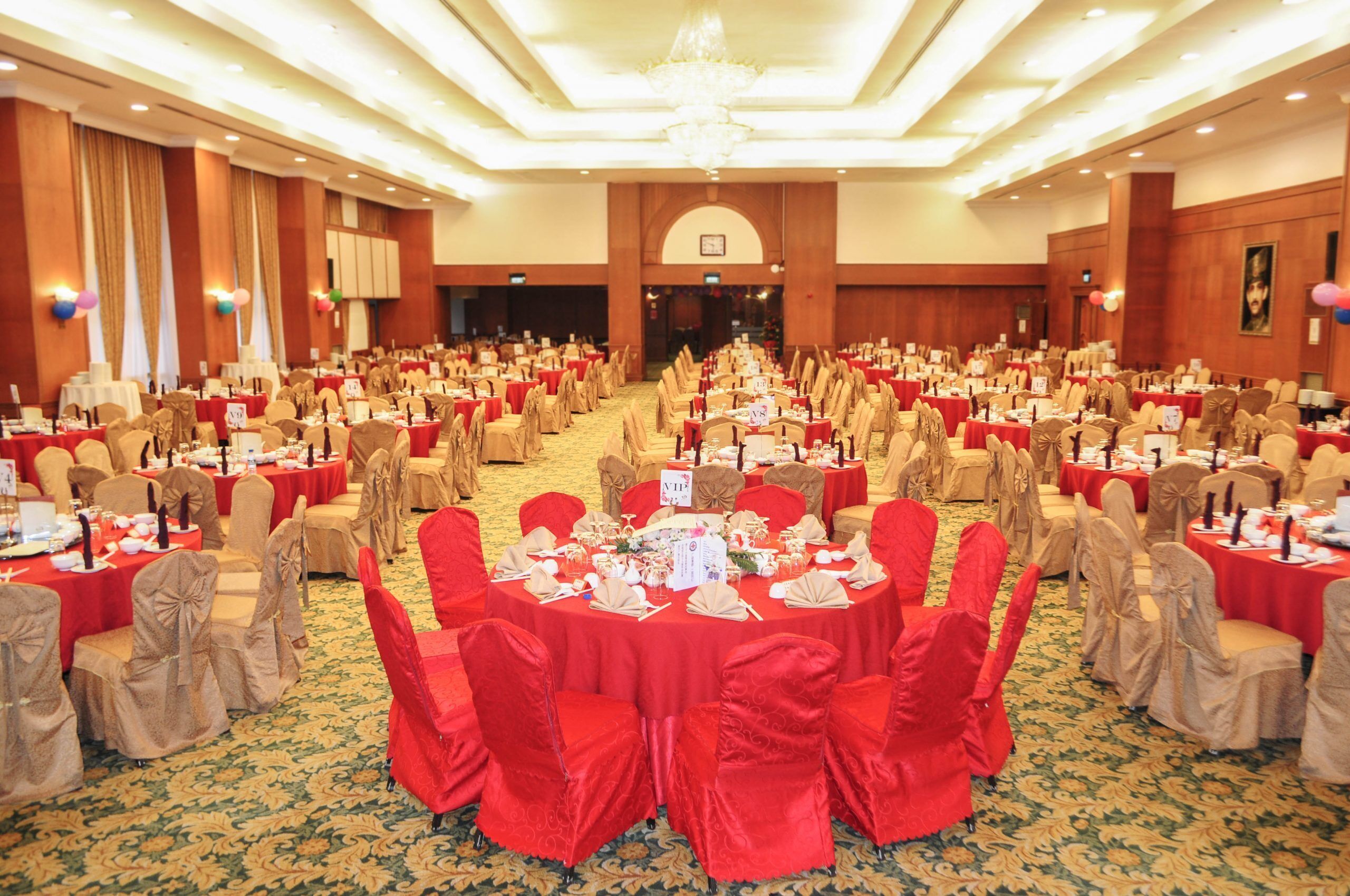 A banquet hall with round tables, red tablecloths, and beige chairs.
