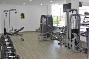 Un gimnasio con diversos equipos de ejercicio, incluyendo mancuernas, una prensa de banca y máquinas de pesas.