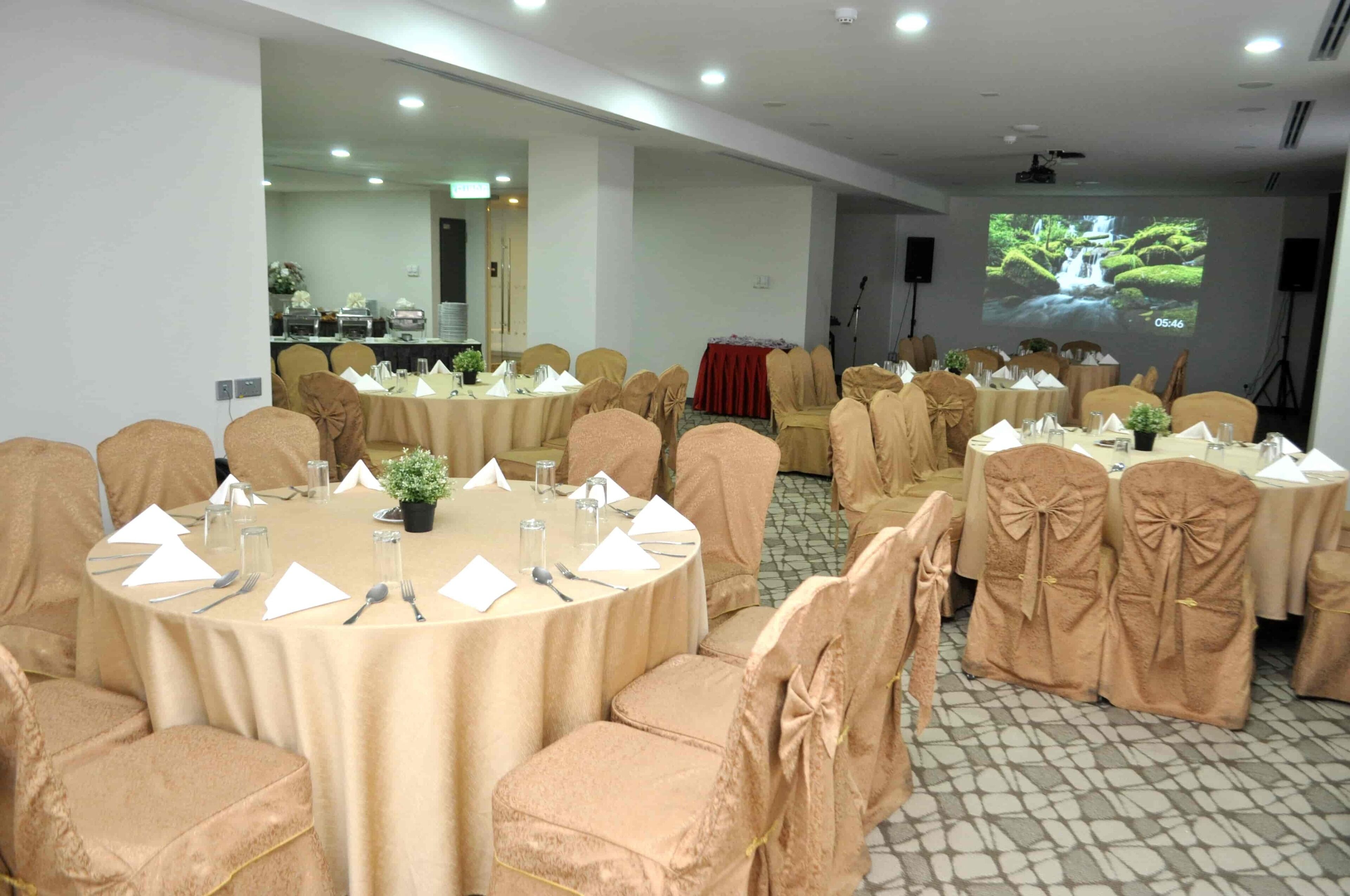 A conference room with round tables, chairs, and a projection screen displaying a waterfall.