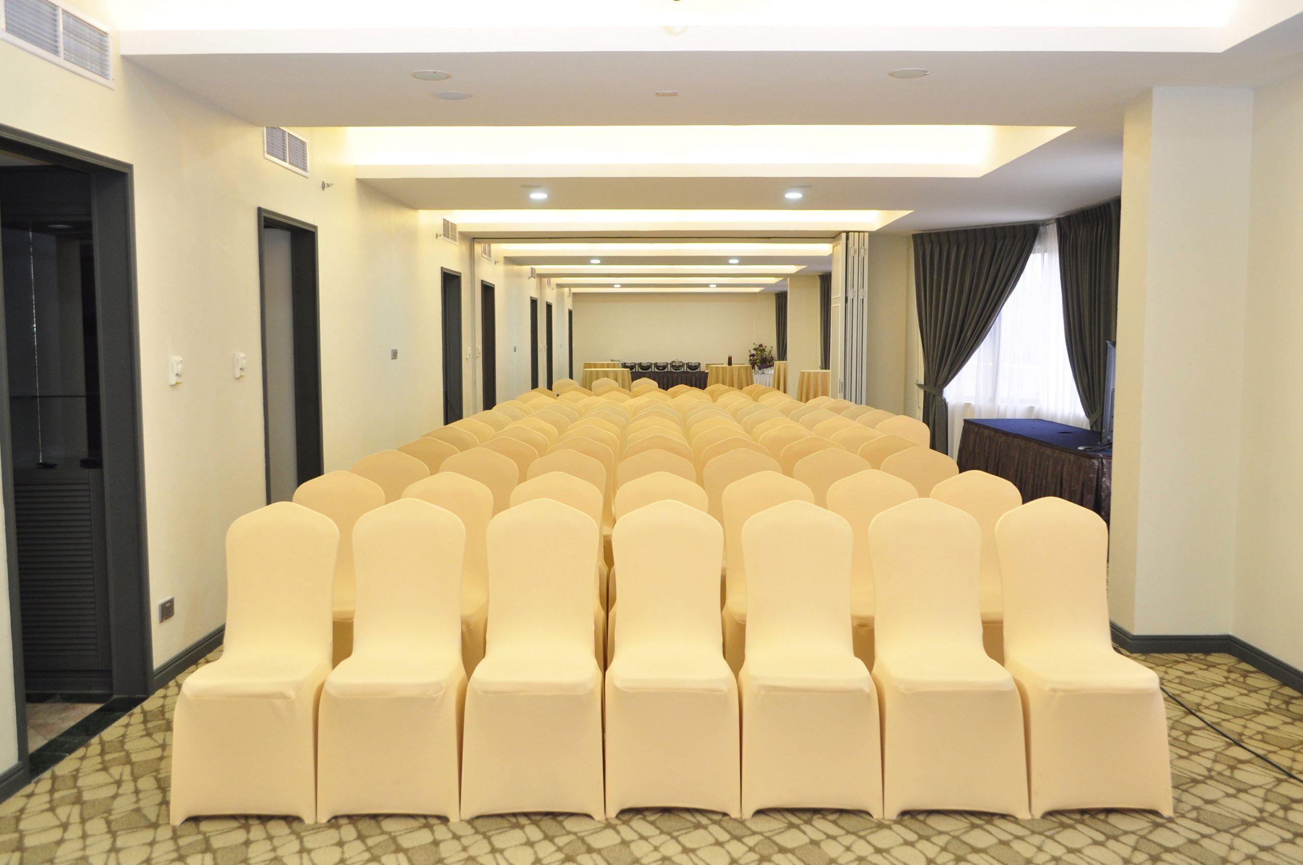 Une salle de conférence avec des rangées de chaises beiges, une longue table au centre et un tapis à motifs.